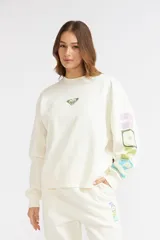 Buzo Roxy modelo Hey Yeah, color crudo de cuello redondo, manga larga con estampado grande multicolor en la manga izquierda y pequeño logo en el pecho.