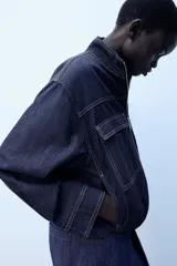 Cazadora bomber de denim oscuro con cuello subido, manga larga y bolsillos frontales con solapa. Presenta cierre frontal de cremallera y bajo elástico.