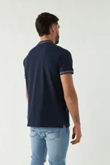 Remera polo negra de manga corta con ajuste regular. Presenta cuello y puños con ribete a rayas en gris y bordó. El logo de la marca está estampado en el pecho.