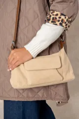 Cartera de gamuza color beige con correa ajustable de cuero sintético marrón, bolsillo frontal con solapa y cierre superior.