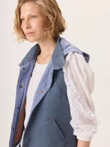 Chaleco con capucha, presenta una espalda de pelo sintético en color marrón oscuro con etiqueta de cuero negra y una capucha de tela tipo denim azul. Diseño original con mezcla de texturas.