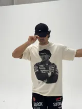 Remera de algodón color beige con estampa fotográfica frontal de Ayrton Senna con su traje de piloto de Fórmula 1. Presenta un corte oversize y cuello redondo.