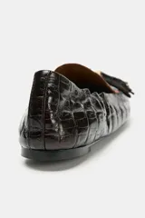 Mocasín de mujer en cuero con textura de piel de cocodrilo, color negro. Presenta detalle de borlas en el empeine, ribetes en contraste y punta redonda.