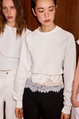 Sudadera crop de cuello redondo y manga larga con puños elásticos. Presenta un diseño de doble capa con un top interior satinado y un bajo decorado con encaje a tono.