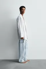 Blazer de corte relajado confeccionada en tejido de lino. Presenta cuello chal, manga larga, bolsillos de plastrón en la parte frontal y cierre cruzado con botones.