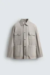 Cazadora de corte relajado confeccionada en tejido de algodón compacto con efecto lavado. Presenta cuello de solapa, manga larga con puños abotonados y cierre frontal de botones. Incluye cuatro bolsillos frontales: dos de plastrón con solapa en el pecho y dos bolsillos dobles de plastrón en la cadera.