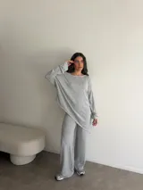 Conjunto gris melange compuesto por un buzo de cuello bote amplio y corte asimétrico con bolsillos, y un pantalón largo de corte recto y holgado.