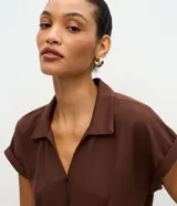 Blusa color marrón con cuello solapa, mangas cortas con vuelta y cierre frontal de botones. Cuenta con un diseño texturizado y un lazo para anudar en el bajo.