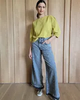 Pantalón de jean de corte wide leg, con diseño de costuras verticales frontales y ruedo desflecado con detalle de franja oscura en el borde inferior.