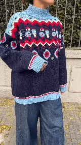 Buzo de tejido jacquard con cuello alto, diseño estampado con motivos de granja, árboles y figuras geométricas en colores azul marino, celeste, rojo y crema. Presenta puños y ruedo acanalados en color celeste.