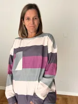 Remera de manga larga en tejido liviano con diseño de rayas anchas en tonos fucsia, gris y crudo. Corte recto y cómodo con bolsillo delantero.