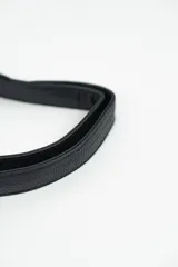 Cartera tipo riñonera o bandolera de cuero sintético negro con textura granulada, forma de media luna y detalles de tachas plateadas en el borde inferior. Cuenta con cierre metálico plateado y correa ajustable.