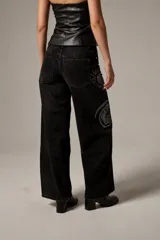 Pantalón jean de corte recto y tiro bajo, color negro gastado, con detalles de apliques de strass formando diseños de estrellas, soles y flores.