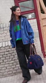 Bolso amplio de gamuza azul con manijas largas de cuero marrón. Cuenta con bolsillos laterales, uno con clip, cierre posterior y un bolsillo interno amplio. Presenta detalle de bandera y logo bordado en los laterales.