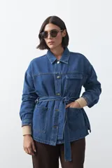 Sobrecamisa de jean color negro con silueta relajada, cuello camisero, cierre frontal con botones metálicos, bolsillos frontales y cinturón ajustable en la cintura.