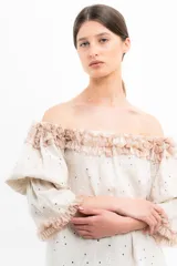Blusa color crema con pequeños lunares marrones, escote off-shoulder con volados y mangas 3/4 abullonadas con volados en los puños.