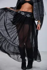 Pollera larga de microtul transparente, color negro, con diseño fluido y volados en el ruedo. Cuenta con una cintura elástica adornada con tachas circulares metálicas.