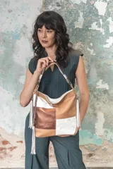 Bolso tipo hobo de cuero vacuno en patchwork de color caramelo, blanco tiza y cobre metalizado. Tiene un asa corta fija y una correa larga ajustable y desmontable con mosquetones metálicos. El interior está forrado en tela y cuenta con un bolsillo con cierre y un porta celular.