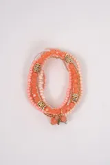 Set de pulseras elásticas compuesto por múltiples hileras de cuentas en tonos rosados, corales y blancos, intercaladas con separadores metálicos dorados con strass y un dije colgante en forma de abeja.