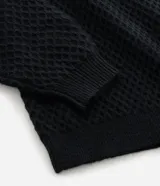 Buzo de punto negro con textura geométrica tipo colmena, cuello alto y mangas largas con puños ajustados.