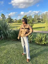 Cardigan de lana color camel con cuello polo, botones frontales y detalles de caballos hechos a mano en cuero negro. Presenta una franja horizontal negra tejida en el pecho y en las mangas.