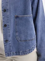 Campera de jean azul con corte holgado, cuello clásico, cierre frontal con botones y bolsillos delanteros amplios.