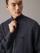 Sweater azul con textura tipo waffle, cuello alto, cierre frontal con cremallera metálica, puños y bajo acanalados, y logo pequeño en el pecho.