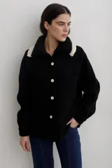 Camisa de paño de lana, color negro, con cuello tejido en contraste y cierre frontal de botones claros. Presenta bolsillos frontales y diseño de corte recto.