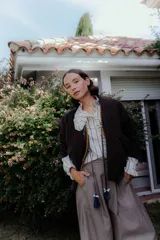 Chaqueta acolchada de algodón en color marrón oscuro, con diseño de matelassé, corte holgado y cierre frontal con cordones decorativos terminados en borlas azules.