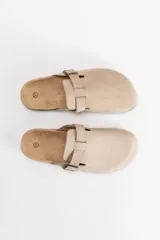 Zueco de estilo casual en color beige, con capellada de material sintético tipo gamuza, ajuste mediante hebilla metálica lateral y suela con detalle de corcho.