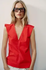 Top rojo de popelín con escote en V pronunciado, mangas sisa y pespuntes en contraste. Cuenta con tirantes finos cruzados y lazada en la espalda.