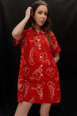Vestido corto beige con estampado botánico en negro, cuello camisero, mangas cortas y cierre frontal con botones.