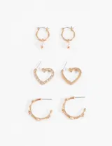 Set de tres pares de aros plateados: un par con forma de corazón con strass, un par tipo argolla con apliques y un par tipo argolla con dije de perla.