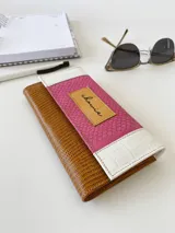 Billetera de cuero con diseño tricolor que combina texturas: cuerpo principal en marrón con textura tipo lagarto, solapa central en fucsia con textura granulada y detalles en blanco con textura tipo cocodrilo. Incluye una etiqueta central de cuero en color tostado con la marca grabada y cierre con broche.
