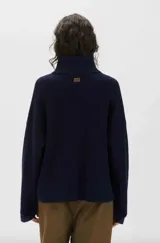 Sweater de punto color azul marino, con cuello alto, cierre frontal parcial y mangas largas anchas.