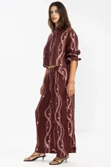 Camisa corta de lino color borgoña con estampado de cadenas y flores rosadas. Tiene cuello clásico, mangas largas y cierre frontal con botones.