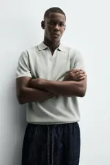 Jersey de punto color verde oliva, de calce relajado (relaxed fit), con cuello solapa y abertura frontal en forma de V. Es de manga corta y presenta acabados en rib en puños y ruedo.