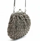 Bolso de mano tejido artesanalmente en hilo gris con detalles de canutillos en tono peltre. Presenta una boquilla metálica estilo vintage con cierre a presión y una cadena larga plateada para llevar al hombro.