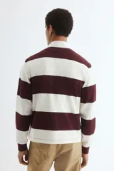 Remera tipo polo de manga larga con diseño a rayas horizontales en color bordó y blanco. Presenta cuello inglés, tapeta con botones ocultos y puños acanalados.