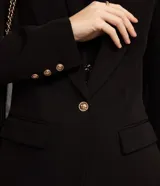 Blazer negro de crepé con cuello solapa, manga larga, bolsillos con solapa y cierre de un solo botón dorado.