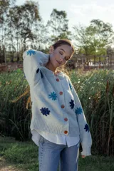 Cardigan de lana color celeste con cuello redondo, cierre frontal con botones color naranja y flores bordadas en azul y celeste.