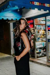 Chaleco negro de cuero con detalles de crochet en gris y rojo. Presenta un diseño sin mangas y un aplique de corazón bordado en el frente.