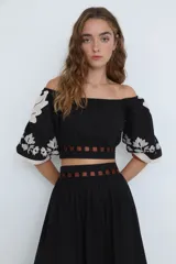 Top corto negro con escote bardot, mangas cortas abullonadas con bordado floral blanco y detalle de recortes con tiras horizontales color café en la cintura.