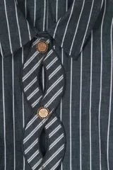 Camisa corta a rayas verticales grises y blancas, con cuello clásico y mangas largas. Presenta un diseño trenzado en el frente con botones dorados y aberturas.