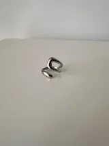 Anillo de diseño abierto y forma sinuosa, fabricado en acero quirúrgico con acabado pulido brillante.