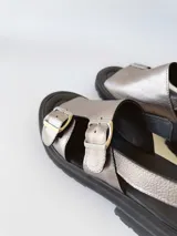 Sandalias de cuero color peltre con plataforma y suela track color negro. Presentan dos tiras anchas con hebillas plateadas y tira trasera ajustable.