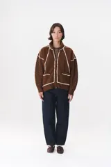 Campera de tejido de punto color marrón con destellos de lurex, corte oversize y cierre frontal. Presenta detalles de costuras y terminaciones en color crema, cuello alto y bolsillos frontales.