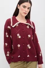 Saco de punto color bordó con bordados artesanales de flores en tonos rosados. Presenta un cuello con detalle de volados en color crema y cierre frontal con botones. De silueta amplia y cómoda.