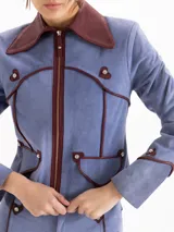 Chaqueta de gamuza color celeste con cuello camisero y detalles de ribetes en cuero marrón. Cuenta con cierre frontal y bolsillos aplicados con solapa.