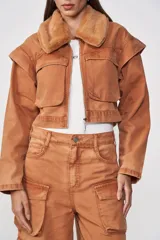 Chaqueta corta color caramelo con cuello de piel sintética, cierre frontal con cremallera, bolsillos con solapa y charreteras en los hombros.